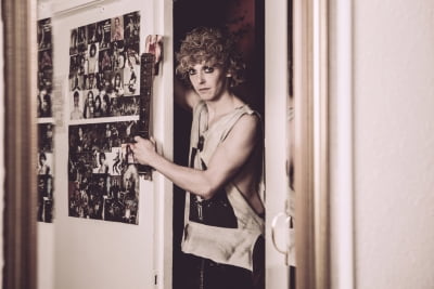 Andrew Polec posing as Strat in his dressing room, his inspirational idols on the wall, and the neck of a broken guitar in his hands