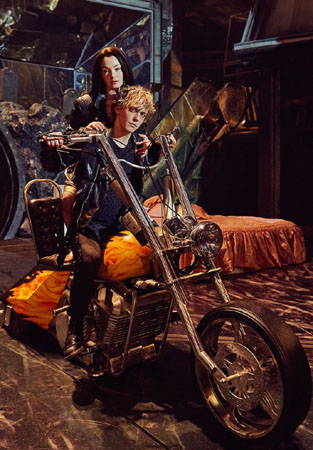 Strat (Andrew Polec) and Raven (Christina Bennington) pose on a motorbike
