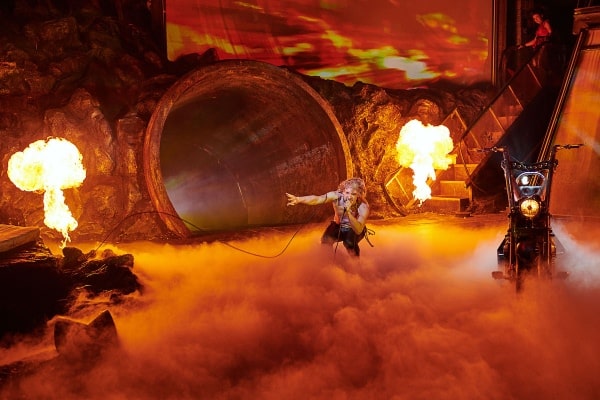 Andrew Polec as Strat, crouching as orange smoke pools and rolls on the stage