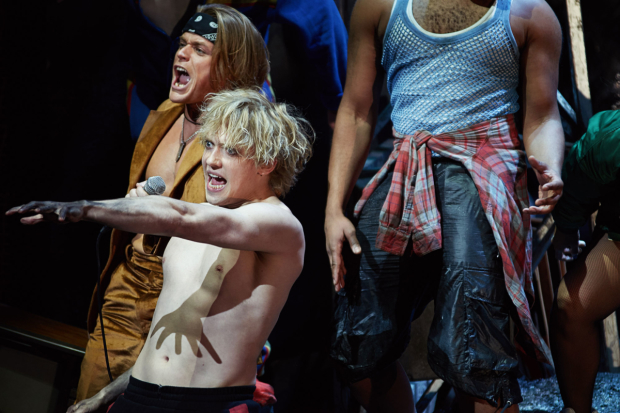 photo from Bat Out Of Hell The Musical. Andrew Polec as Strat is in the foreground, motorcycle grease-covered hand outstretched as he sings. Behind him, Giovanni Spano as Ledoux
