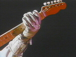 a silver-gloved hand grips the neck of an electric guitar