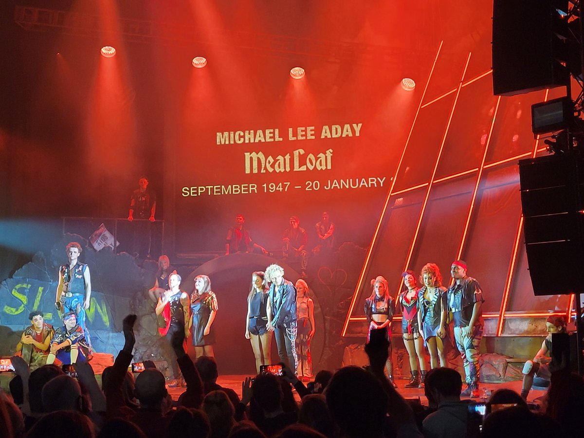 The stage at the end of a performance of Bat Out Of Hell The Musical. The cast take their bows, and behind them is an enormous projection: Michael Lee Aday. Meat Loaf. September 1947 - 20 January 2022.